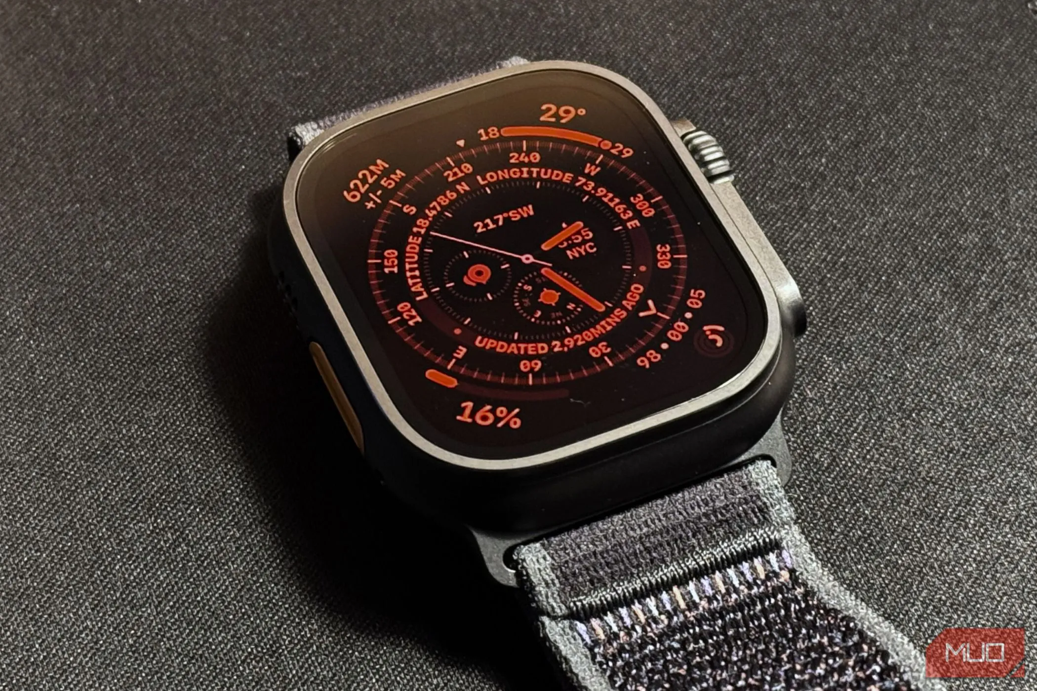 Apple Watch Ultra 2 đang hiển thị chế độ ban đêm màu đỏ trên mặt đồng hồ Wayfinder, đặt trên thảm đen