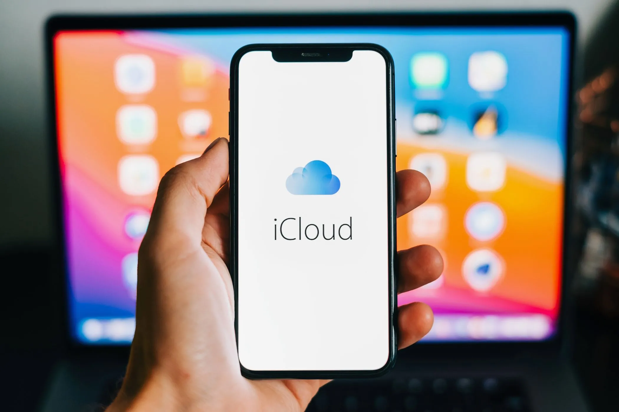 Biểu tượng iCloud trên màn hình iPhone với MacBook ở hậu cảnh