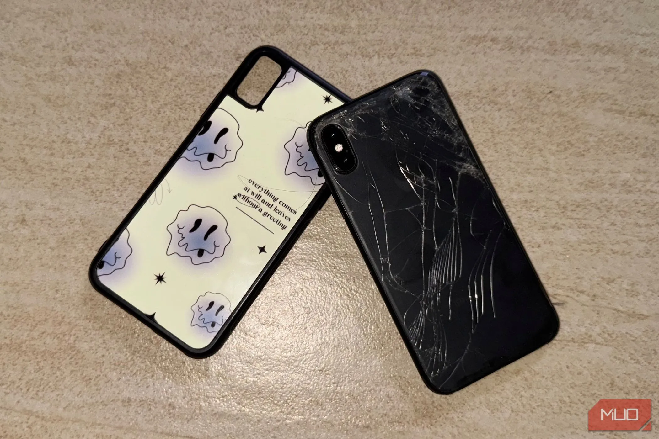 Chiếc iPhone X với mặt lưng kính bị nứt nằm trên sàn, cạnh một chiếc ốp lưng, minh họa độ mong manh của vật liệu này.
