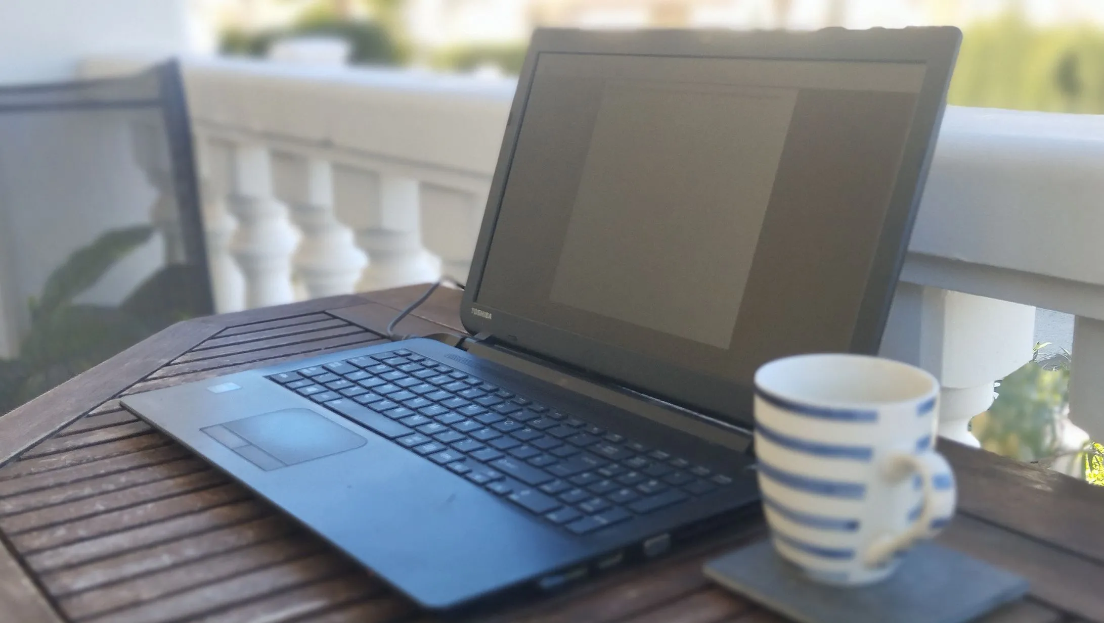 Chiếc laptop Toshiba cũ được tái chế đặt trên bàn làm việc cạnh tách cà phê, tượng trưng cho một cỗ máy năng suất hiệu quả.