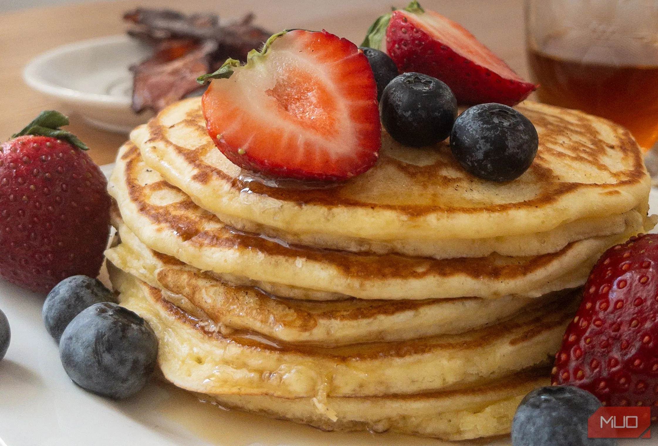 Đĩa bánh pancake được xếp chồng cao, phủ sốt và trái cây, chụp ở góc nghiêng 45 độ để thể hiện rõ các lớp và độ sâu của món ăn.