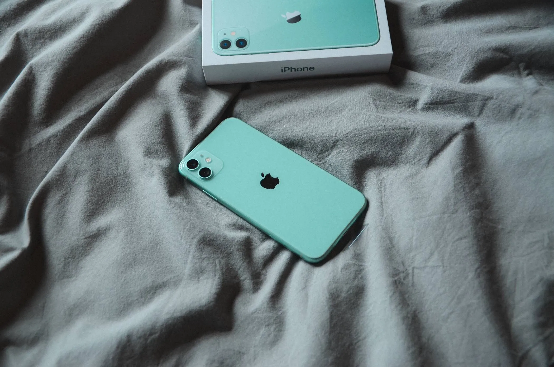 Điện thoại iPhone đang nằm trên chăn hoặc ga trải giường, minh họa nguy cơ khi sạc điện thoại trên bề mặt kín, dễ tích nhiệt