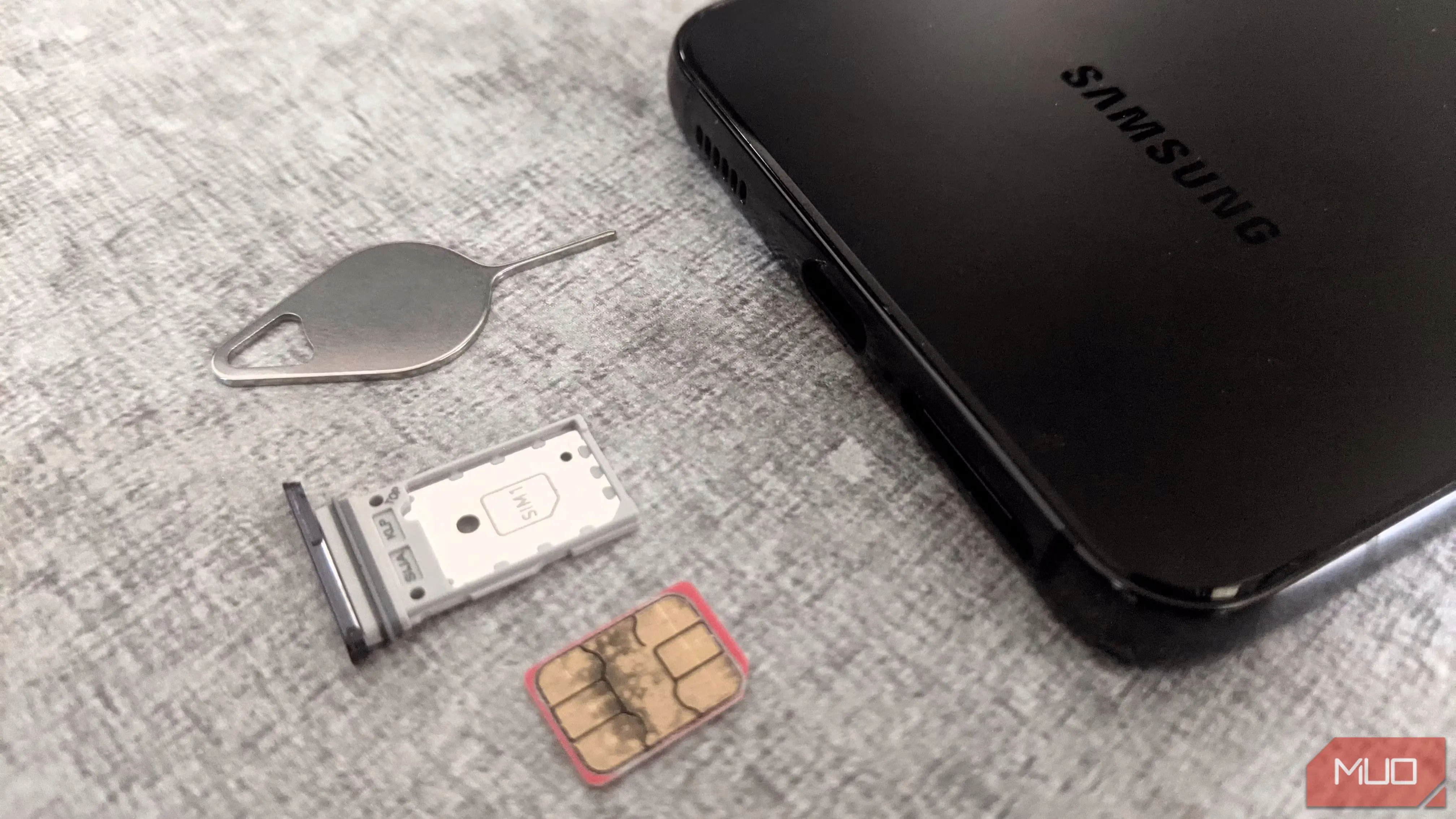 Điện thoại Samsung, khay SIM và dụng cụ tháo SIM trên bề mặt phẳng.