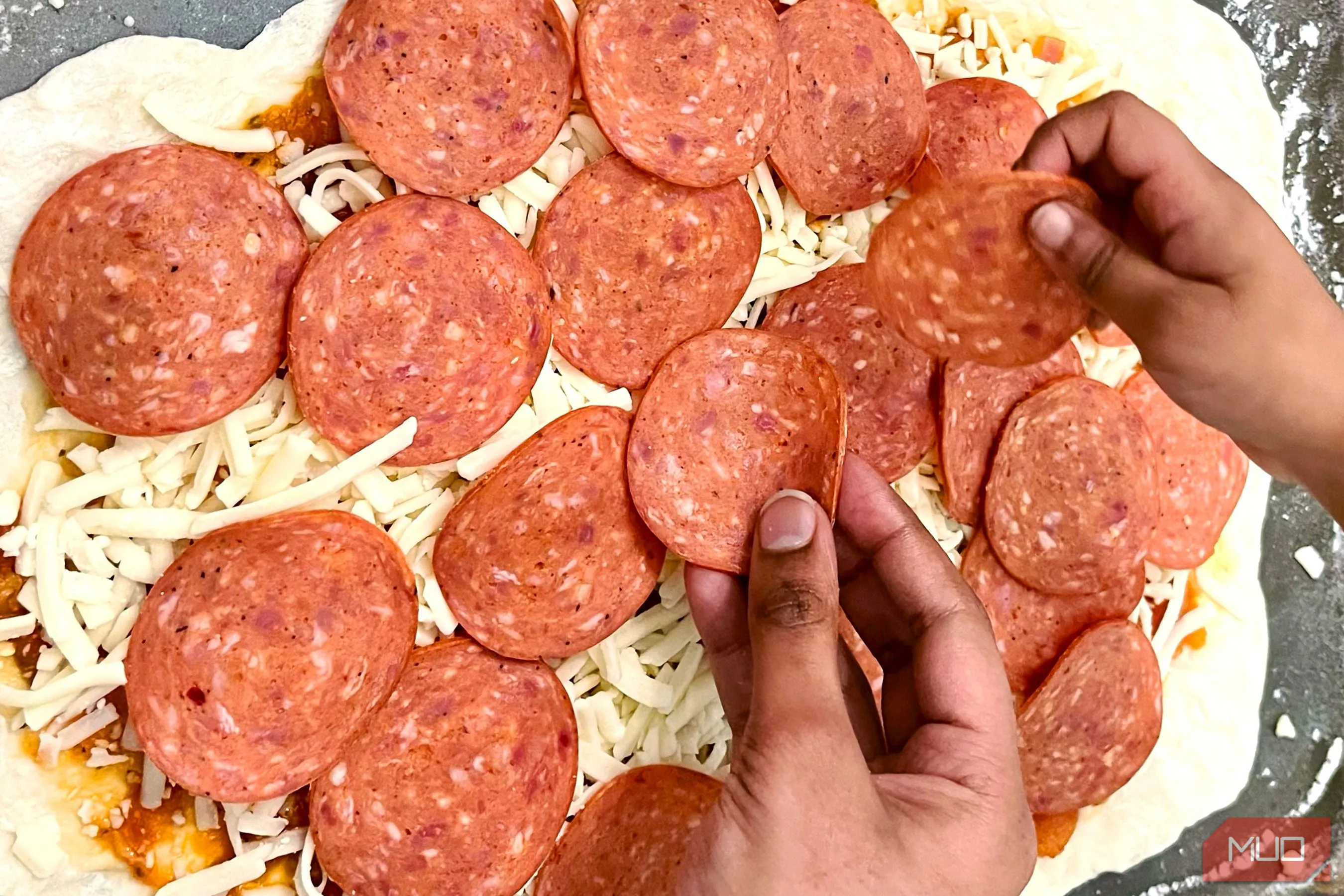 Đôi bàn tay đang rải topping trên chiếc bánh pizza chưa nướng, tạo nên câu chuyện về quá trình chuẩn bị món ăn tại nhà.
