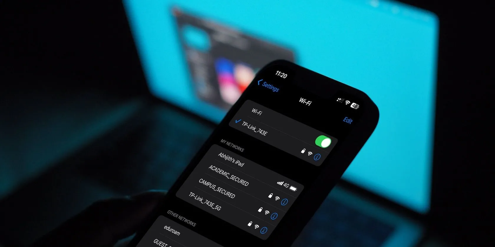 Giao diện menu Wi-Fi trên iPhone với máy Mac phía sau, thể hiện cách chọn mạng Wi-Fi công cộng an toàn.