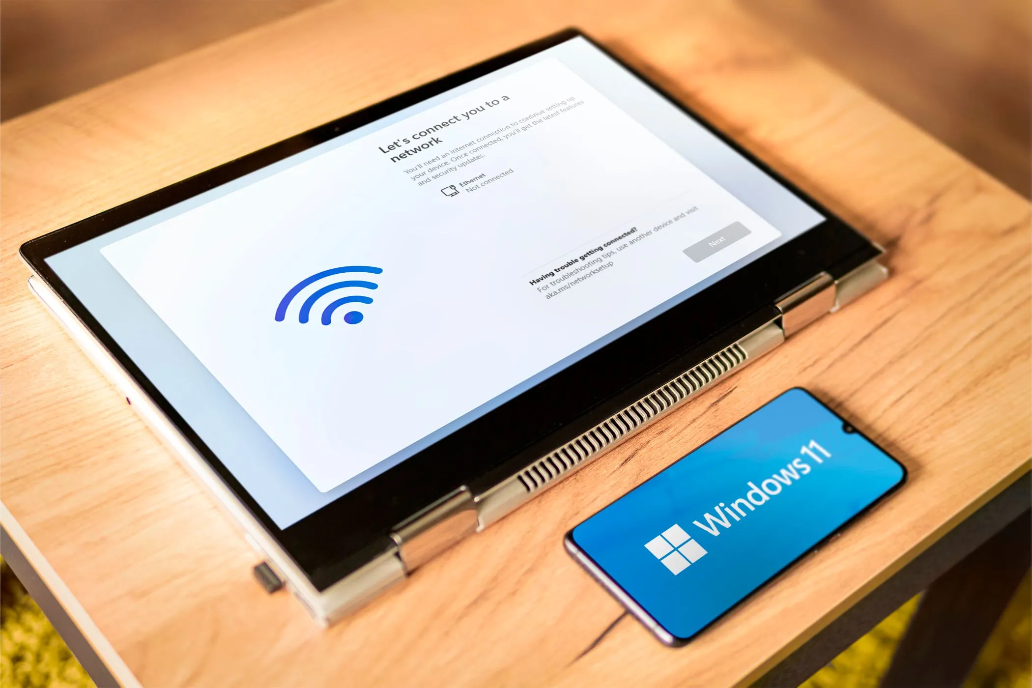 Hình ảnh một chiếc laptop và điện thoại thông minh cùng hiển thị biểu tượng Windows 11, tượng trưng cho khả năng điều khiển máy tính Windows từ xa bằng điện thoại Android