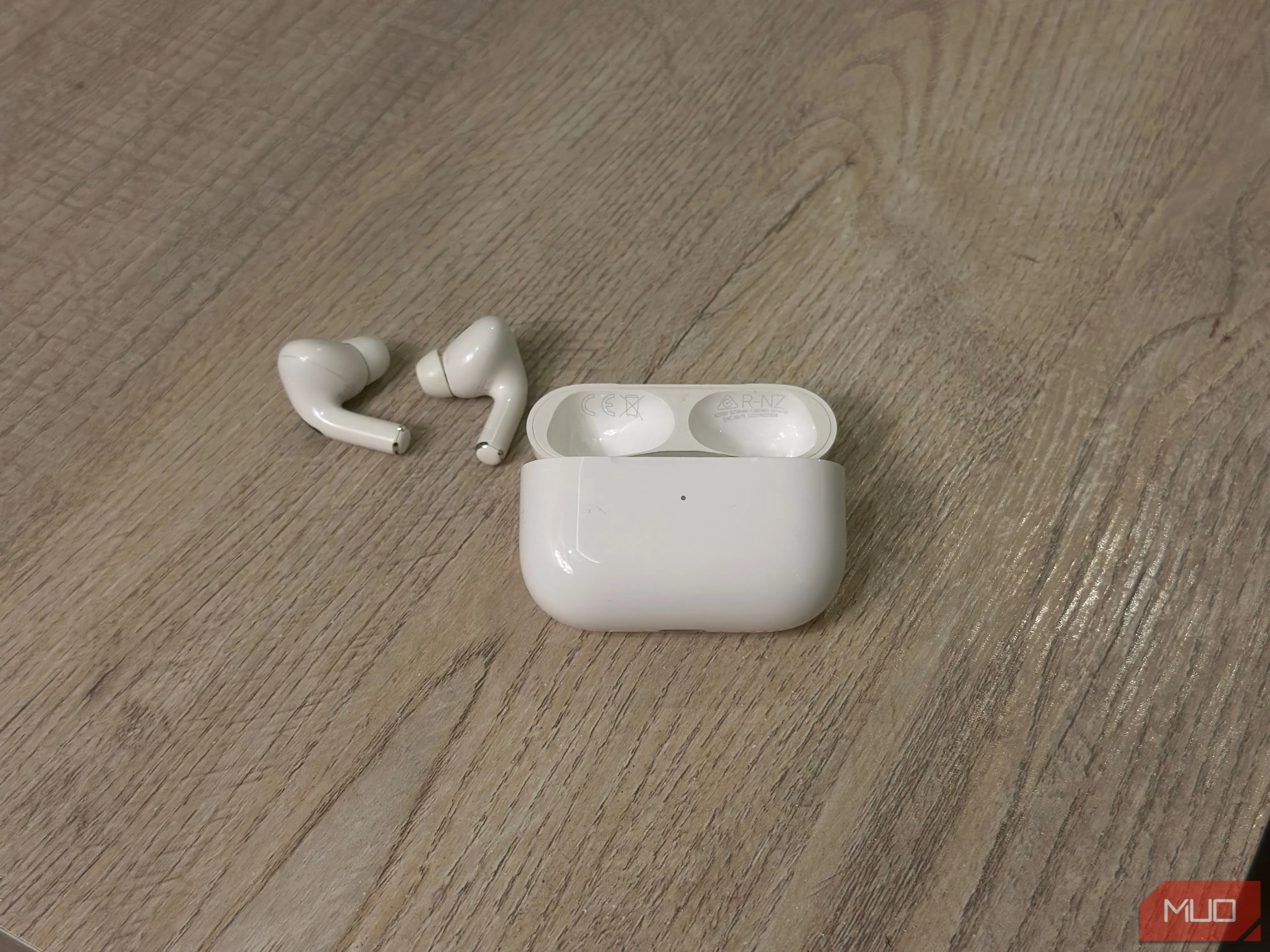 Hộp sạc AirPods và tai nghe đặt trên mặt bàn, minh họa vị trí số model và số serial được in bên trong nắp hộp sạc để dễ dàng tra cứu.
