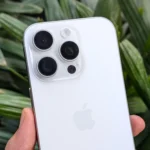 iPhone 16 Pro màu trắng trong tay trước cây xanh, minh họa thiết kế camera nổi bật