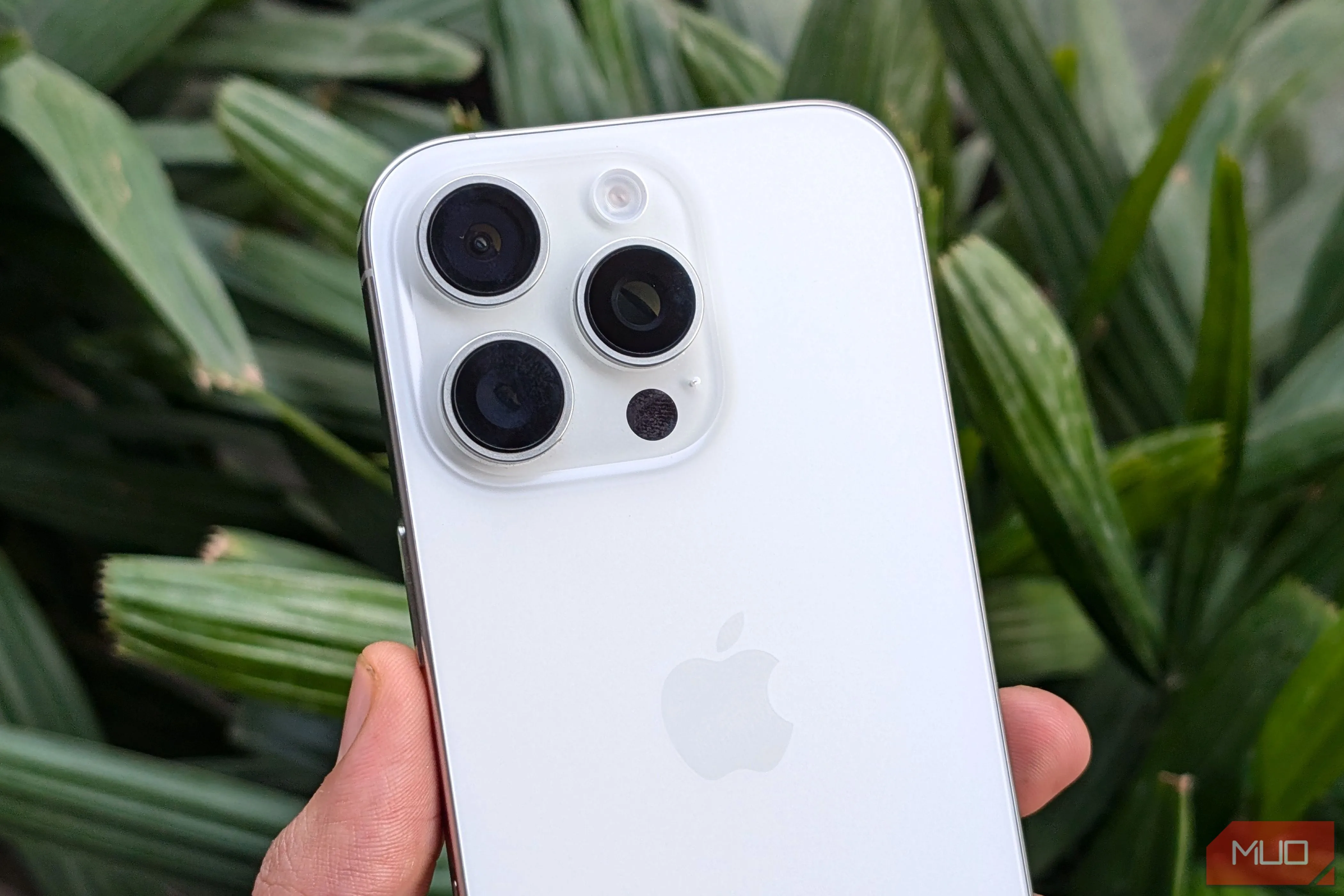 iPhone 16 Pro màu trắng trong tay trước cây xanh, minh họa thiết kế camera nổi bật