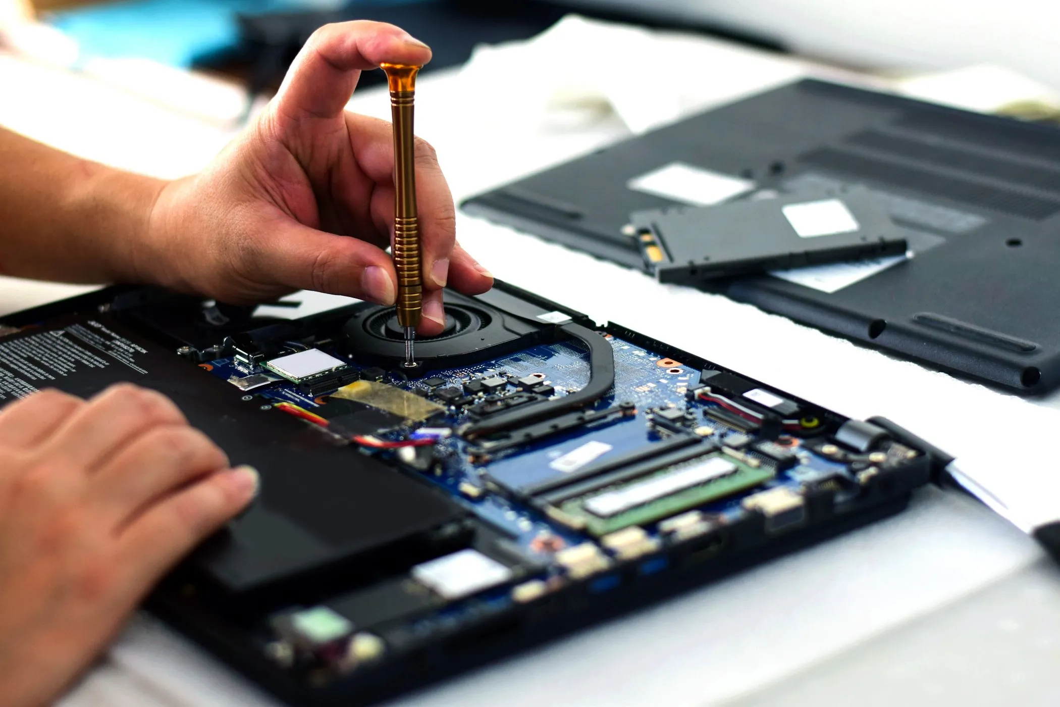 Kỹ thuật viên đang sửa chữa bo mạch chủ laptop bằng tuốc nơ vít, làm nổi bật sự phức tạp của việc sửa chữa laptop mỏng