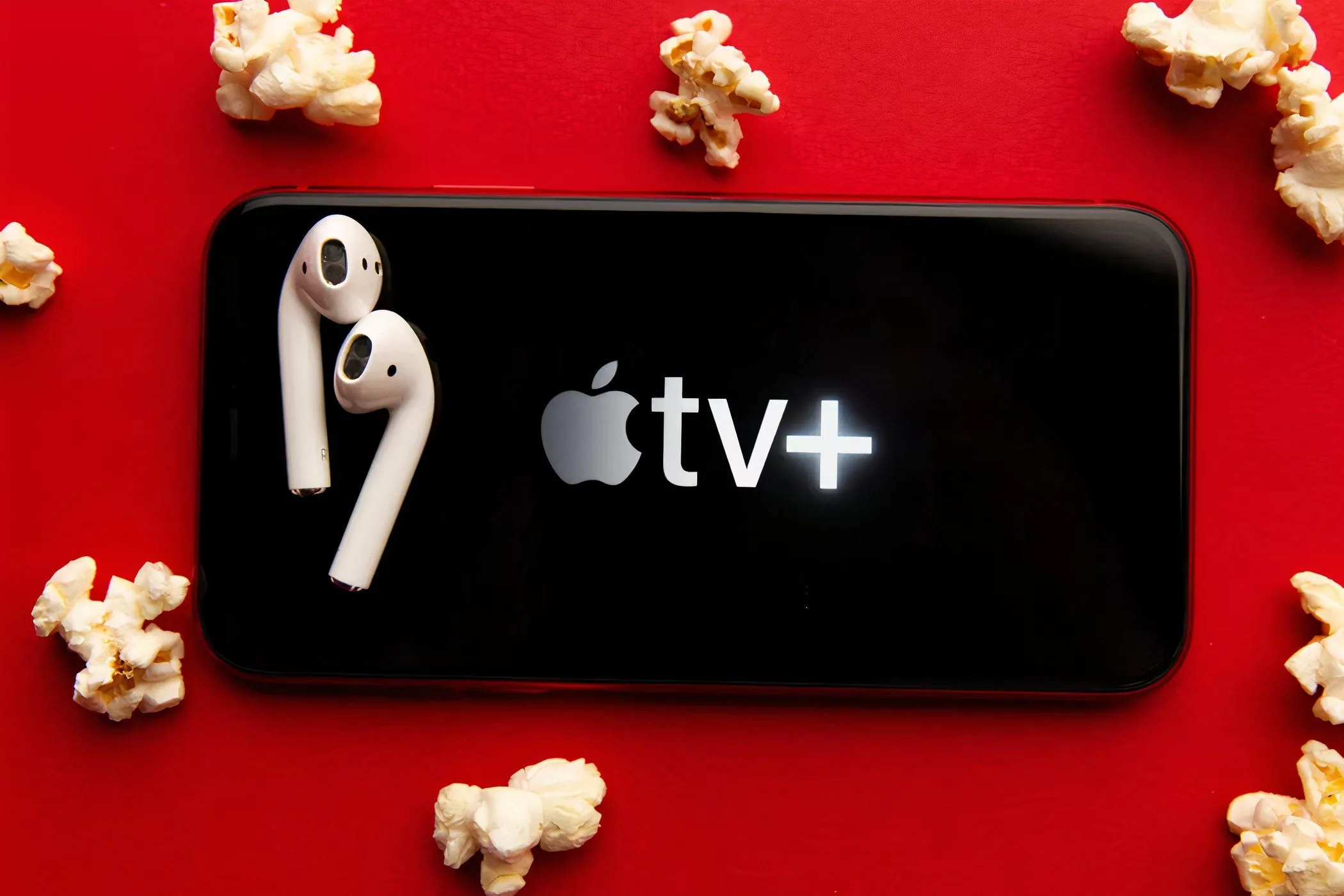 Màn hình điện thoại hiển thị logo Apple TV+ cùng bắp rang bơ và tai nghe, minh họa trải nghiệm xem phim tiện lợi.