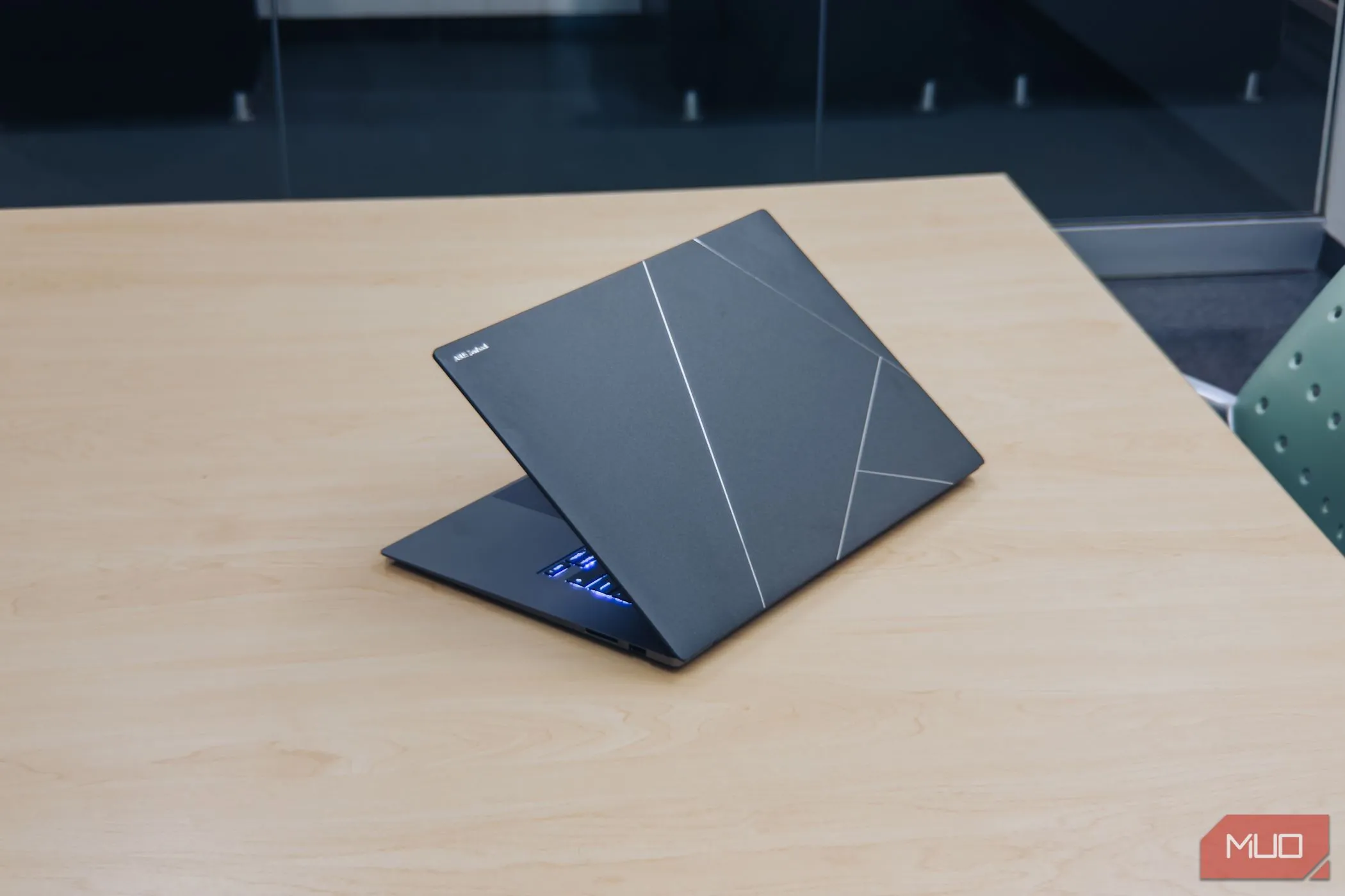 Mặt lưng laptop ASUS Zenbook S 16 OLED với lớp vỏ Ceraluminum sang trọng trên bàn gỗ