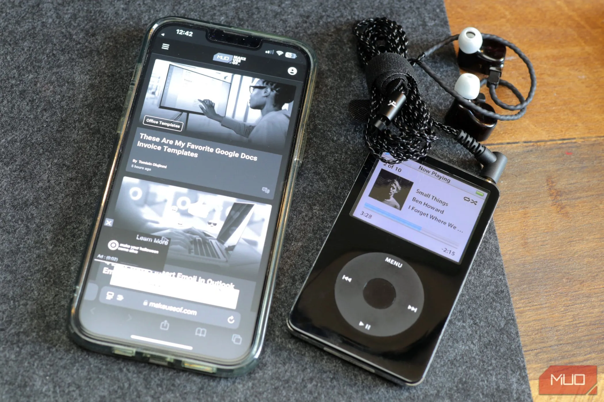 Một chiếc iPod màu đen và iPhone 13 màu xám trên bàn nỉ, gợi nhớ thiết bị nghe nhạc cổ điển
