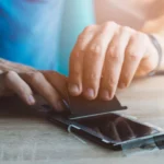Người đàn ông đang cẩn thận dán miếng bảo vệ màn hình lên điện thoại iPhone để chống trầy xước.