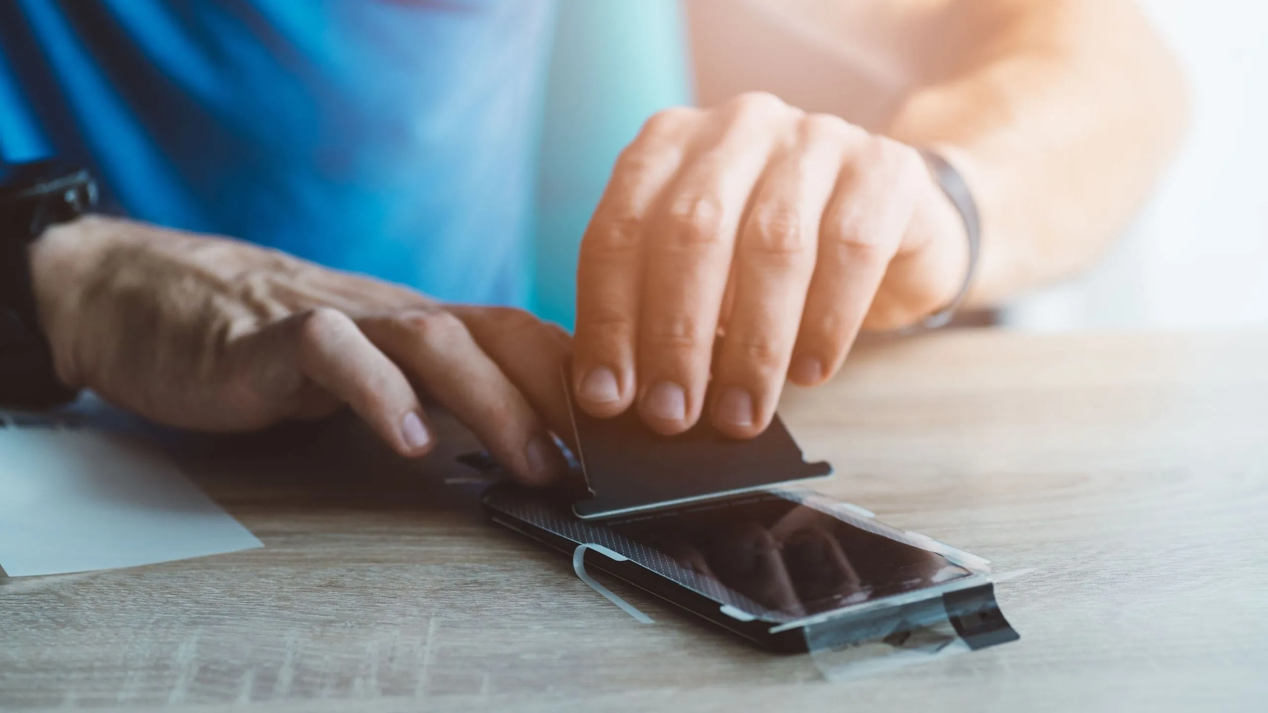 Người đàn ông đang cẩn thận dán miếng bảo vệ màn hình lên điện thoại iPhone để chống trầy xước.