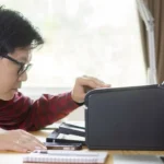 Người đàn ông đang kiểm tra máy in trên bàn làm việc, có thể là gặp sự cố in ấn trên Windows.