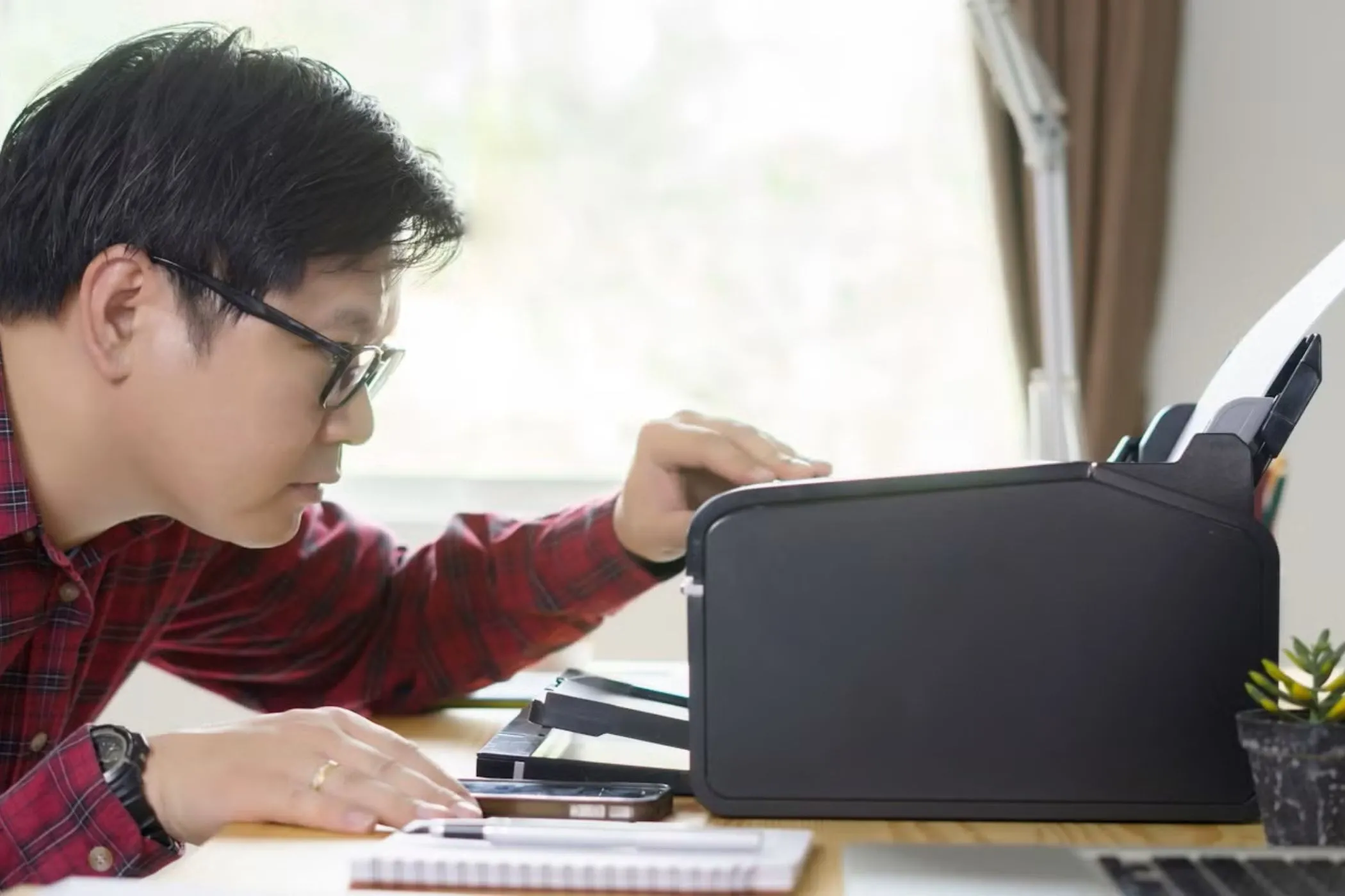 Người đàn ông đang nhìn vào máy in trên bàn làm việc, tượng trưng cho khả năng kết nối thiết bị ngoại vi