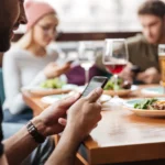 Người đàn ông sử dụng điện thoại tại quán cà phê trong lúc ăn uống cùng bạn bè để tìm mã Wi-Fi.