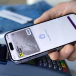 Người đàn ông thanh toán không tiền mặt bằng điện thoại iPhone tại quầy thu ngân, thể hiện sự tiện lợi của giao dịch kỹ thuật số và mối liên hệ với dữ liệu khách hàng thân thiết.