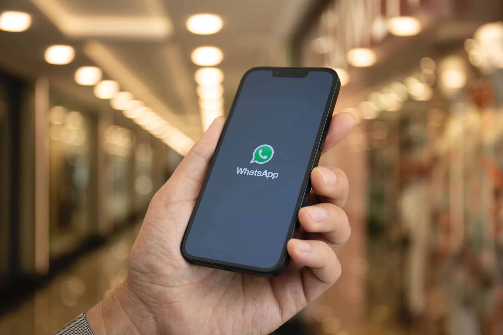 Người dùng đang cầm điện thoại xem logo WhatsApp với tính năng phiên âm tin nhắn thoại