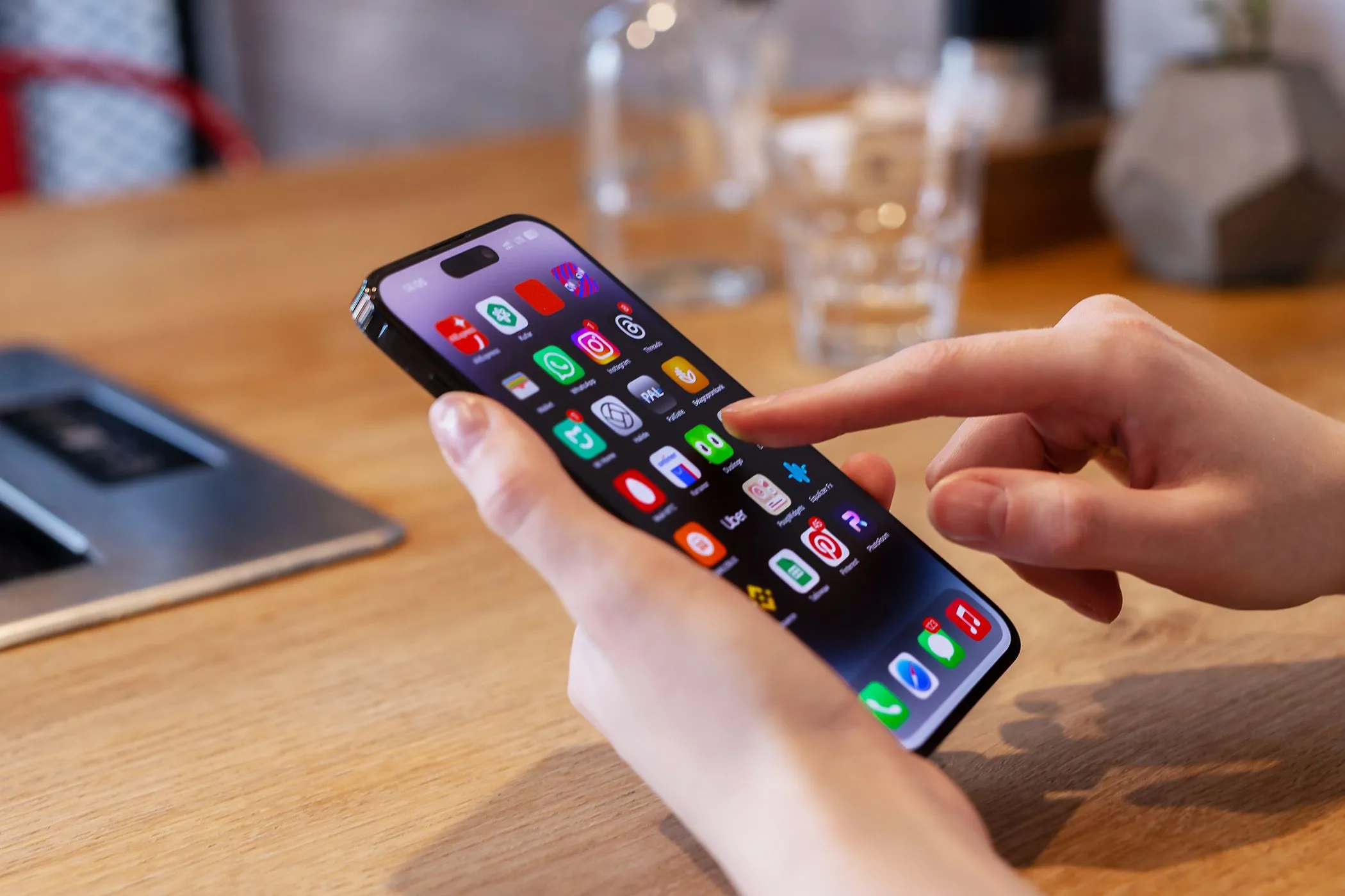 Người dùng đang sử dụng điện thoại iPhone trên bàn với ly nước phía sau, minh họa cho việc sử dụng thiết bị di động