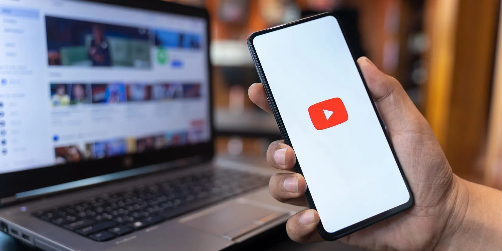 Người dùng đang xem ứng dụng YouTube trên điện thoại, phía sau là giao diện website YouTube trên máy tính