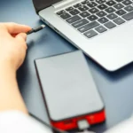 Người phụ nữ sạc điện thoại từ laptop bằng cáp USB-C, minh họa việc thiết bị ngoại vi làm chậm quá trình sạc laptop
