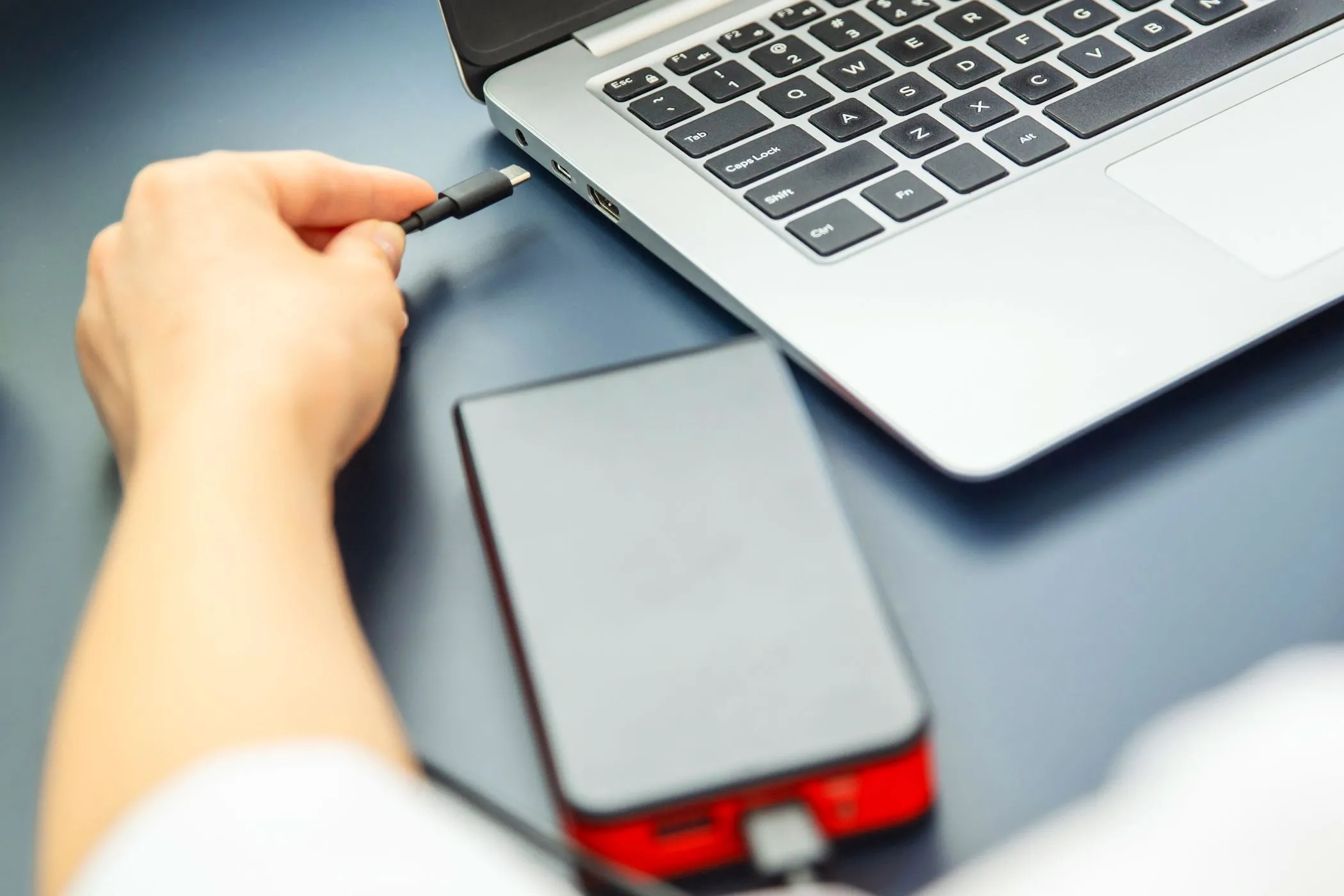 Người phụ nữ sạc điện thoại từ laptop bằng cáp USB-C, minh họa việc thiết bị ngoại vi làm chậm quá trình sạc laptop