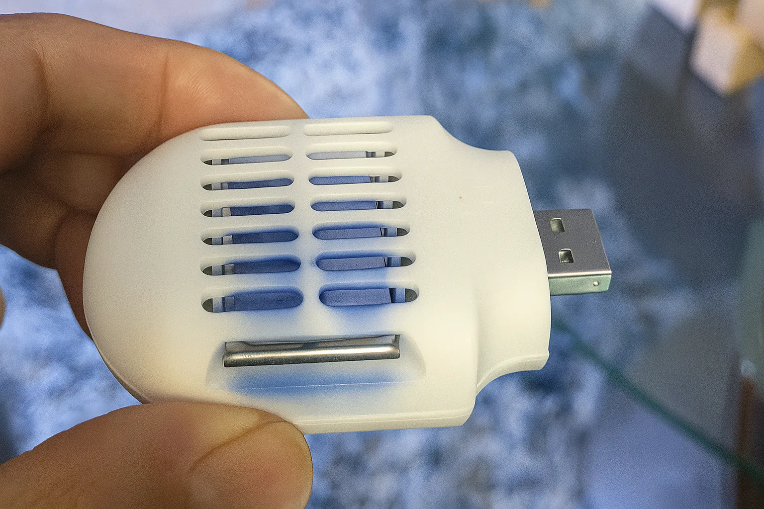 Thiết bị đuổi muỗi USB Moskiller nhỏ gọn màu trắng, được cầm trên tay, có thể cắm vào cổng USB xe hơi để chống côn trùng.